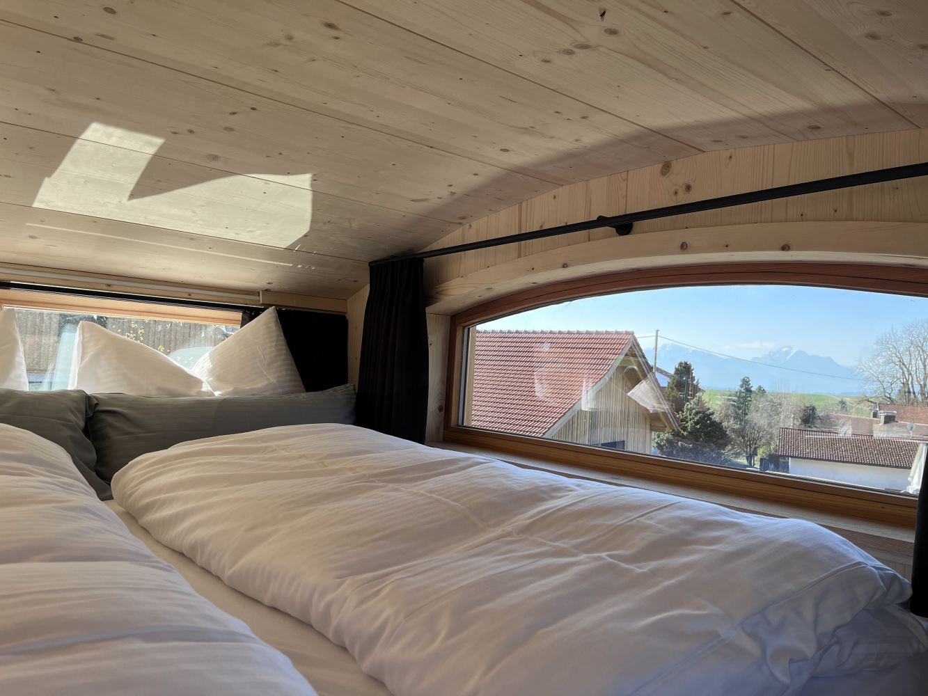 Schlafbereich im Tiny House mit großem Fenster und Blick über Dächer und Landschaft des Allgäus.