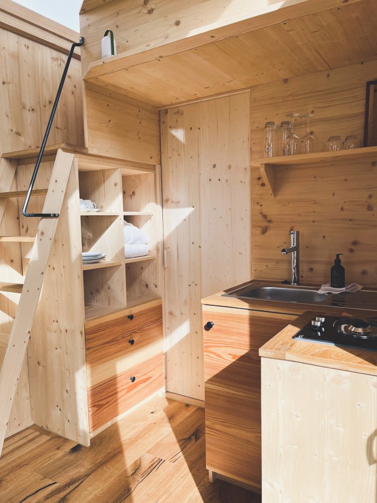 Holzverkleideter Küchen- und Stauraumbereich im Tiny House mit Leiter zum Schlafdach.