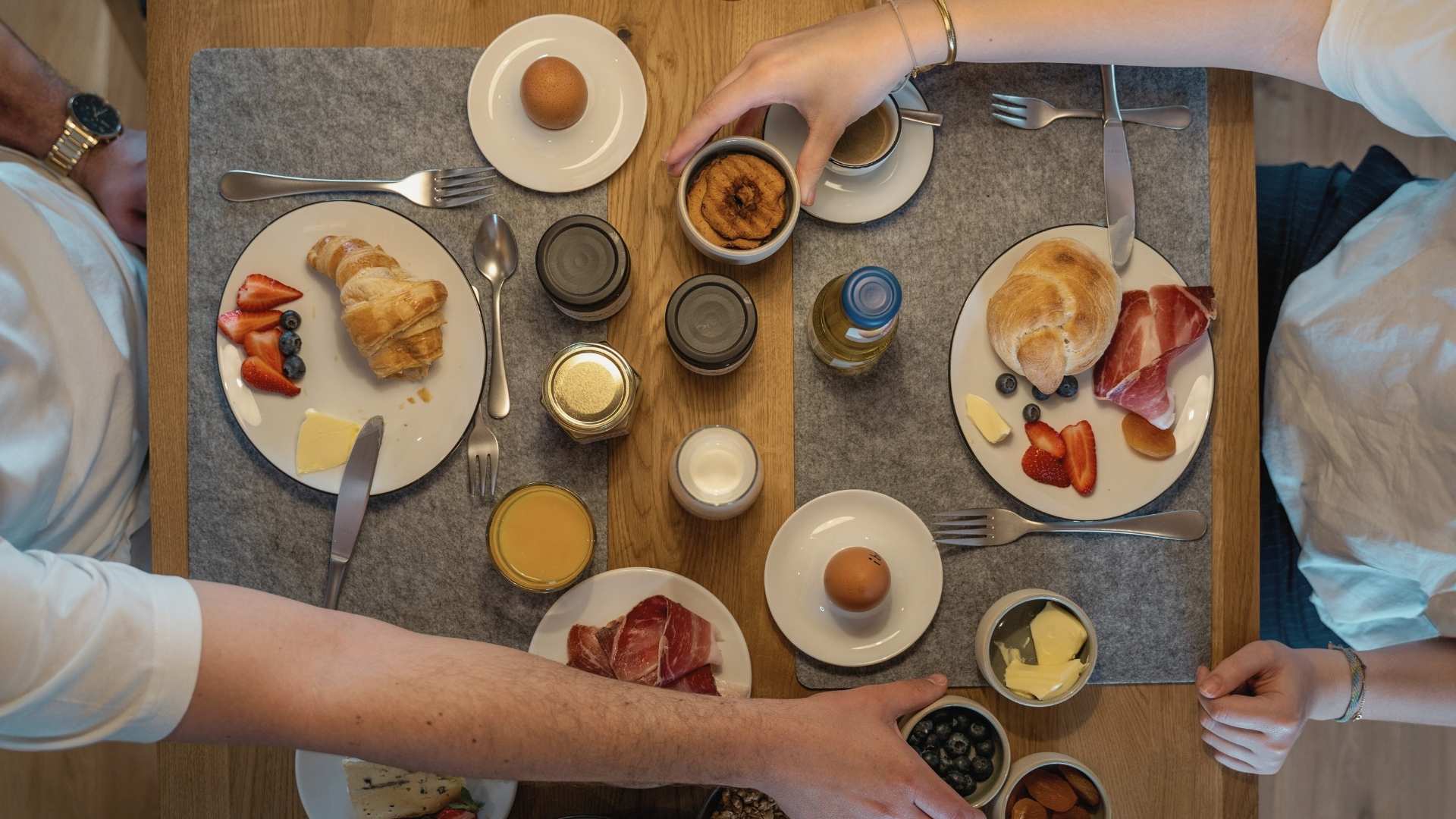 Gedeckter Frühstückstisch mit Croissants, Obst, Aufstrichen und Getränken aus der Vogelperspektive.