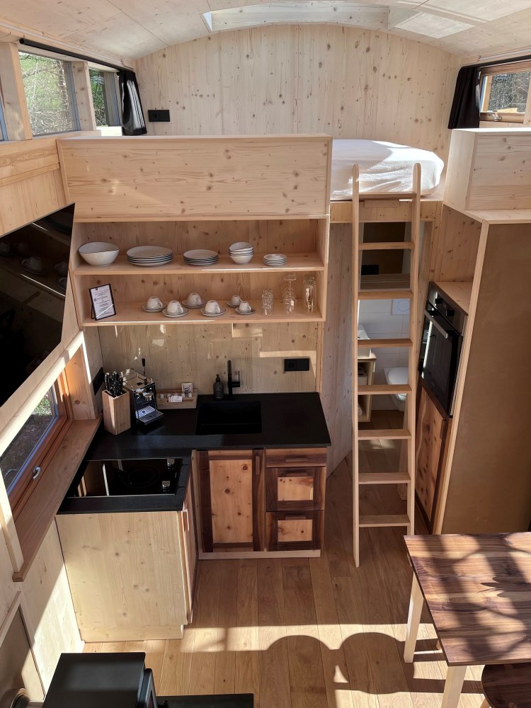 Kompakte Küche und Schlafbereich in einem Tiny House am Mächlerhof mit Holzinterieur, Regalen und Leiter zum Schlafdach.